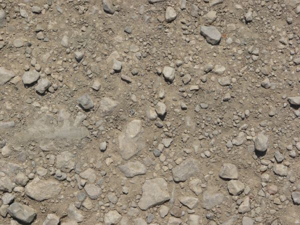 Ground texture of grey rocks of various sizes embedded in rough, grey dirt.